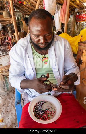 Lokaler Händler, der Souvenirs mit Perlen herstellt, um sie an Touristen auf dem Markt am Diani Beach, Mombasa, Kenia, Afrika, zu verkaufen Stockfoto