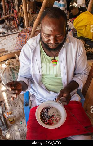 Lokaler Händler, der Souvenirs mit Perlen herstellt, um sie an Touristen auf dem Markt am Diani Beach, Mombasa, Kenia, Afrika, zu verkaufen Stockfoto