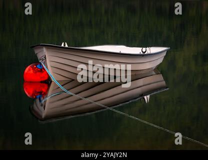 Ein kleines Boot ist an einen Dock gebunden und liegt inmitten eines ruhigen, dunklen Sees. Stockfoto