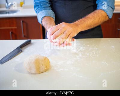 Junger Mann, der mit den Händen einen Weizenmehlteig knete Stockfoto