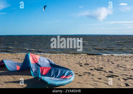 Kotlin, Russland - 20. Juni 2024: Zugdrachen liegt am Ufer, ein Kiteboarder ist im Meer sichtbar, der von einem anderen Power-KI über das Wasser gezogen wird Stockfoto