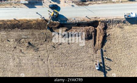 Luftaufnahme der Baustelle mit Baggern, die einen Graben für ein Rohr in der Nähe einer Straße graben. Stockfoto