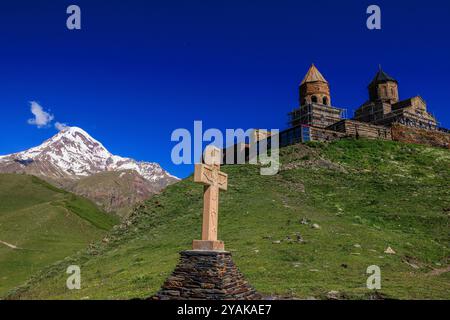 Ein gemeißeltes Steinkreuz neben der gergeti-dreifaltigkeitskirche thront auf einem Hügel über dem Dorf Stiefantsminda mit dem schneebedeckten Berg kazbegi im Hintergrund Stockfoto