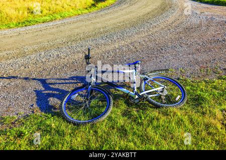 Mountainbike liegt auf grasbewachsener Straße, neben einem Schotterweg in der Landschaft an sonnigen Tagen. Schweden. Stockfoto