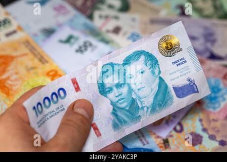 Argentinisches Geld, 10.000 argentinische Pesos-Banknote vor dem Hintergrund anderer Stückelungen in der Hand gehalten Stockfoto