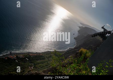 Blick von der Spitze eines Hügels auf den Atlantischen Ozean und seine Küste mit einem kleinen Dorf. Reflexion des Sonnenlichts im Wasser. Faja dos Padres, Madeira, Stockfoto