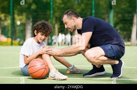 Lehrer hilft Jungen mit Knie Trauma nach dem Basketball spielen Stockfoto