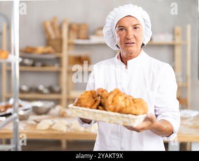 Porträt einer fröhlichen älteren Bäckerin mit Croissants Stockfoto