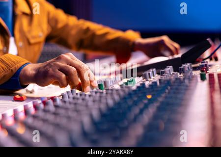 afroamerikanischer Sound-Designer mit Drehknöpfen zum Bearbeiten von Songs im Studio, Bedienpult mit motorisierten Fadern und Drehknöpfen. Musikproduzent erstellt Songs mit Geräten. Nahaufnahme. Stockfoto