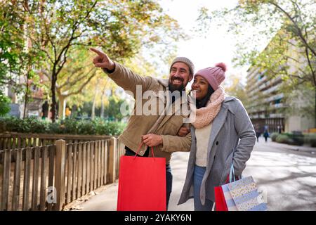 Multiethnische Paare, die in der Stadt spazieren gehen und gemeinsam weihnachtseinkäufe machen, auf Dinge zeigen. Stockfoto