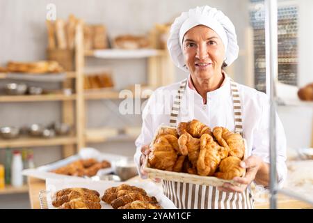 Porträt einer fröhlichen älteren Bäckerin mit Croissants Stockfoto