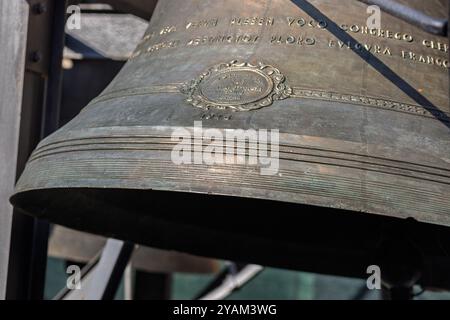 Eine große Bronzeglocke mit verzierten Details und lateinischer Inschrift hängt in einem Kirchturm und zeigt die handwerkliche Kunst der Schöpfung Stockfoto