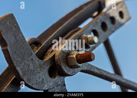 Rostfreie Metallklammer, die Konstruktionselemente mit sichtbarem Gewindeanschluss und blauem Himmel im Hintergrund hält Stockfoto