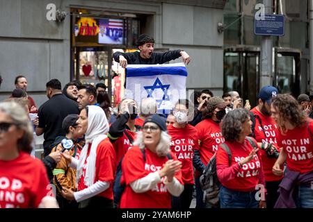 Ein pro-israelischer Gegenprotestierer schwingt während eines Sit-in vor der New Yorker Börse (NYSE) die Flagge Israels über palästinensische Mitglieder der Jewish Voice for Peace, die am 14. Oktober 2024 in New York City gegen die anhaltende Unterstützung und Finanzierung Israels durch die Vereinigten Staaten in ihrem Krieg gegen die Hamas in Gaza protestieren. Die jüdische Stimme für den Frieden, die sich als die größte fortschrittliche jüdische antizionistische Organisation der Welt ausgibt, veranstaltet in den Vereinigten Staaten Proteste, die häufig mit Massenverhaftungen enden. (Foto: Michael Nigro/Pacific Press) Stockfoto