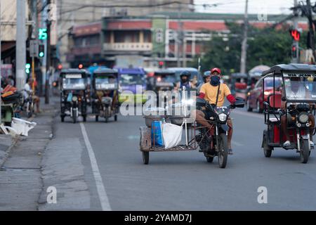 12/10/2024 Cebu City, Philippinen. Ein Mann, der ein motorgetriebenes Benzin-Dreirad fährt. Neben und im Hintergrund sind neuere moderne, weniger umweltbelastende e Stockfoto