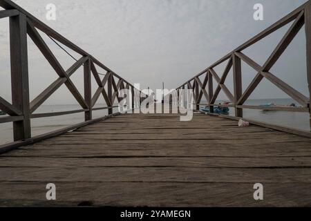 Perspective photo of a wooden jetty on the beach. At the end there is a person squatting Stockfoto
