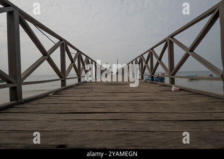 Perspektivisches Foto von einem Holzsteg am Strand. Am Ende hockt eine Person Stockfoto