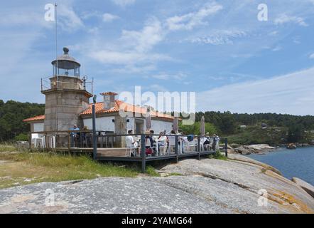 Ein Leuchtturm vor einer Terrasse mit Menschen und Blick auf das Meer, umgeben von Felsen, A Illa de Arousa, La Isla de Arosa, Pontevedra, Galicien, Sp Stockfoto