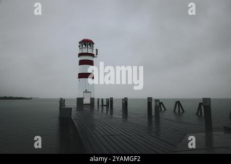 Ein Leuchtturm auf einer Pier unter bewölktem Himmel auf dem Wasser, Podersdorf, Burgenland, Österreich, Europa Stockfoto