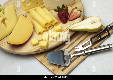 Ein Set verschiedener Käsesorten, Erdbeeren, Birnen und spezielle Käsemesser auf einem Holzbrett Stockfoto