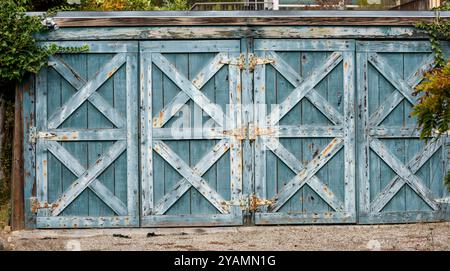 Ein rustikales, verwittertes blaues Holztor mit gekreuzten Holzbalken und rostigen Metallscharnieren. Stockfoto