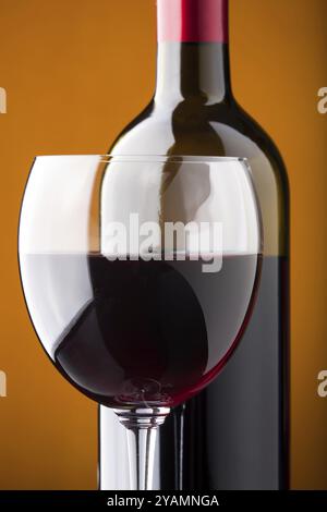 Nahaufnahme eines Glases Rotwein und einer offenen Flasche auf orangefarbenem Hintergrund Stockfoto