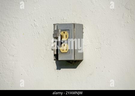 Eine Metallsteckdose für den Außenbereich, die an einer strukturierten weißen Wand befestigt ist und Anzeichen von Verschleiß aufweist. Stockfoto