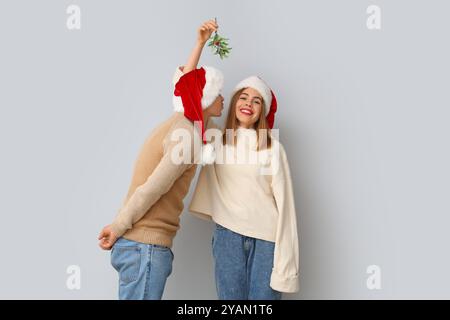 Junges Paar, das sich unter Mistelzweig auf hellem Hintergrund küsst Stockfoto