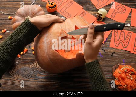 Frau, die Halloween-Kürbis am Holztisch schnitzt Stockfoto