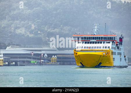 Malerischer Pier mit Booten gegen den Blauen Ozean. Große Fähre segelt auf dem lebhaften Blauen Ozean an sonnigen Tagen Stockfoto