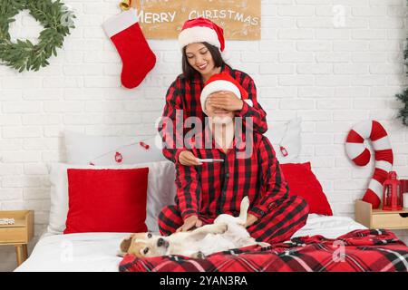 Frau überraschte ihren Mann mit einem Schwangerschaftstest am Weihnachtsabend im Schlafzimmer Stockfoto