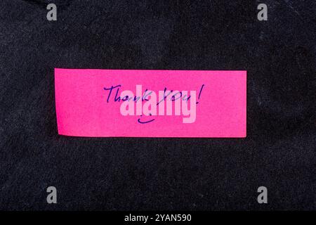 Eine rosafarbene Haftnotiz mit Dankeschön in Blau, platziert auf einer dunklen Steinoberfläche, die Wertschätzung vermittelt. Stockfoto