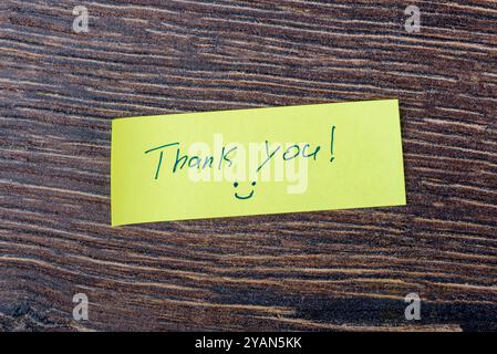 Eine handschriftliche Notiz mit der Aufschrift „Danke You“ auf einem gelben Klebepad, das auf einer Holzoberfläche platziert wurde. Stockfoto