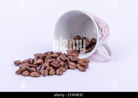 Eine dampfende Tasse frisch gebrühten Kaffees, umgeben von verstreuten Kaffeebohnen auf einem sauberen weißen Hintergrund Stockfoto