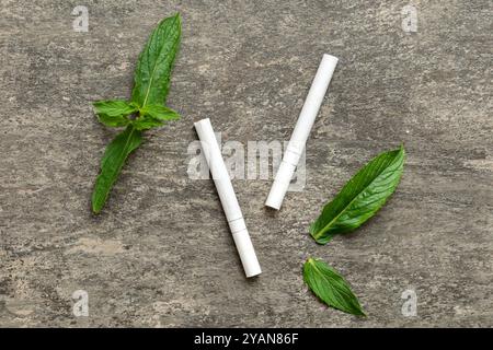 Menthol-Zigaretten und frische Minzblätter auf farbigem Hintergrund, viele Zigaretten gestapelt Draufsicht flach liegend. Stockfoto