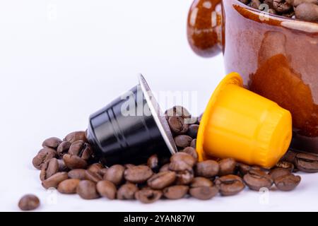 Eine Schüssel Kaffeebohnen mit bunten Kaffeekapseln und verstreuten Bohnen daneben, alle auf weißem Hintergrund für einen frischen Look Stockfoto