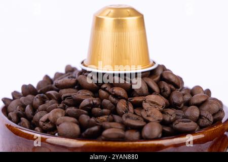 Braune Schüssel mit Kaffeebohnen und einer Kaffeekapsel auf weißem Hintergrund. Die Szene erinnert an die Essenz frisch gebrühten Kaffees Stockfoto