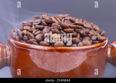 Eine braune Schüssel voller warmer, frisch gerösteter Kaffeebohnen verströmt ein reichhaltiges Aroma, das sich perfekt mit dem eleganten schwarzen Hintergrund abhebt Stockfoto