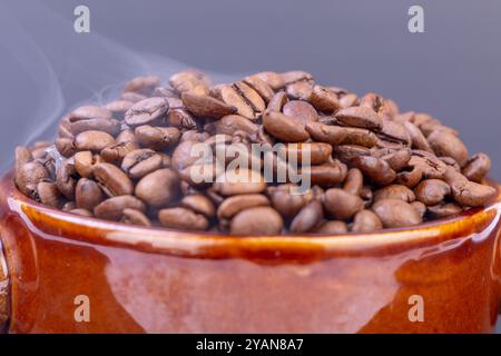 Eine Schüssel mit dampfenden, frisch gerösteten Kaffeebohnen zieht die Aufmerksamkeit auf sich, deren reichhaltiges Aroma vor dem krassen schwarzen Hintergrund strahlt Stockfoto