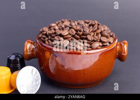 Eine braune Schüssel mit dampfend frisch gerösteten Kaffeebohnen befindet sich neben Kaffeekapseln und bildet einen wunderschönen Kontrast zu einem schwarzen Hintergrund Stockfoto