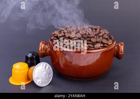 Eine Dampfschale mit frisch gerösteten Kaffeebohnen strahlt reiche Aromen aus, begleitet von Kaffeekapseln, alles vor einem eleganten schwarzen Hintergrund Stockfoto
