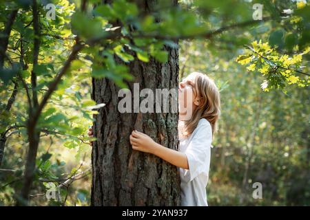 Ein Teenager umarmt einen Baum im Wald. Umarmen und berühren Sie Bäume, um Stress zu reduzieren und sich mit der Natur zu verbinden. Stockfoto