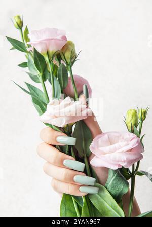 Eine schlanke Hand zeigt lange, pastellfarbene Nägel, während sie sanft einen Blumenstrauß aus zarten rosa Blüten ergreift, was eine ruhige und elegante Ästhetik hervorhebt. Stockfoto