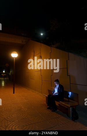 Oung Frau in Geschäftskleidung, die am Laptop arbeitet, während sie am Nachtbahnhof auf den Zug wartet Stockfoto