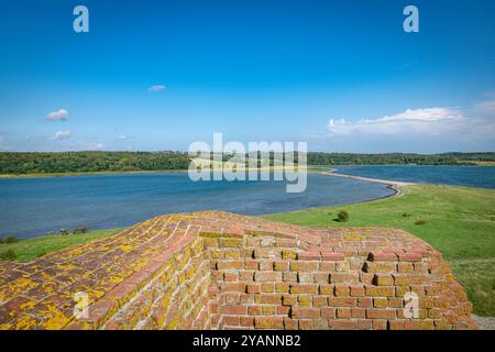 Wunderschöne Seeszene mit einer alten, moosbedeckten Ziegelwand im Vordergrund mit üppigem Grün und einem klaren blauen Himmel im Mols bjerge jutland de Stockfoto