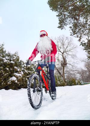 Der Weihnachtsmann fährt im Winter mit dem Fahrrad. Ein Typ mit Bart und Weihnachtsmann-Hut fährt mit einem roten Fahrrad durch den tiefen Schnee Stockfoto