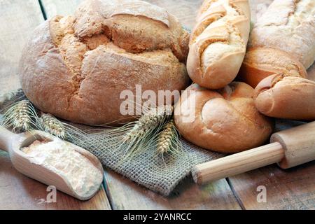 Nahaufnahme von frischem Brot, einer Schüssel Mehl, Weizenkörnern und Spikelets auf Holztisch Stockfoto