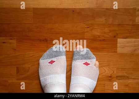 Ein kaukasischer Mann trägt ein paar zerrissene weiße Socken. Zehen ragen aus den Löchern, Blick von oben nach unten, Holzfußboden der Wohnung. Stockfoto