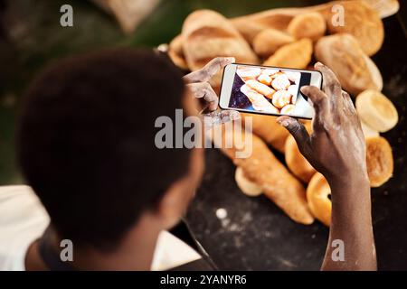 Schwarzer Mann, Bäckerei oder höher mit Telefonbildschirm für Fotos, Bilder oder Brot im Geschäft. Draufsicht, männliche Person oder Bäcker mit Mobiltelefon-Smartphone für Stockfoto
