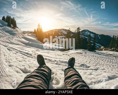 Beine Ansicht eines jungen Mannes, der den Sonnenuntergang auf schneehohen Bergen sieht - Travel Influencer erstellt Inhalte für sein soziales Netzwerk Profil - Winterurlaub Stockfoto